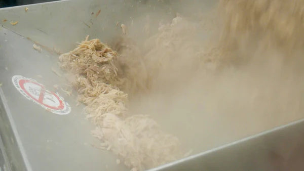 一台大型工业搅拌机正在加工肉丝,产生了一团蒸汽。这里的气氛繁忙而实用,强调食品生产。