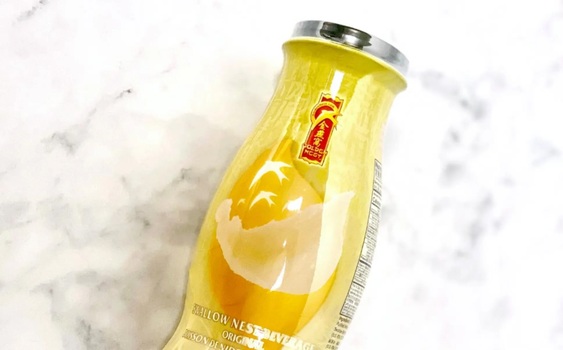 大理石表面的黃色飲料瓶,銀色瓶蓋。以大膽的紅色和金色標籤為特色,描繪飛翔中的鳥兒。優雅而高級的感覺。
