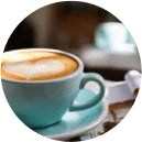 A teal cup of cappuccino with heart-shaped foam sits on a table, creating a cozy and inviting atmosphere with blurred background and warm tones.