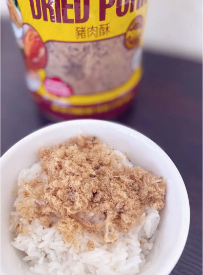 A bowl of white rice topped with dried pork floss. A container labeled "Dried Pork" is in the background, reflecting a simple, savory meal setting.