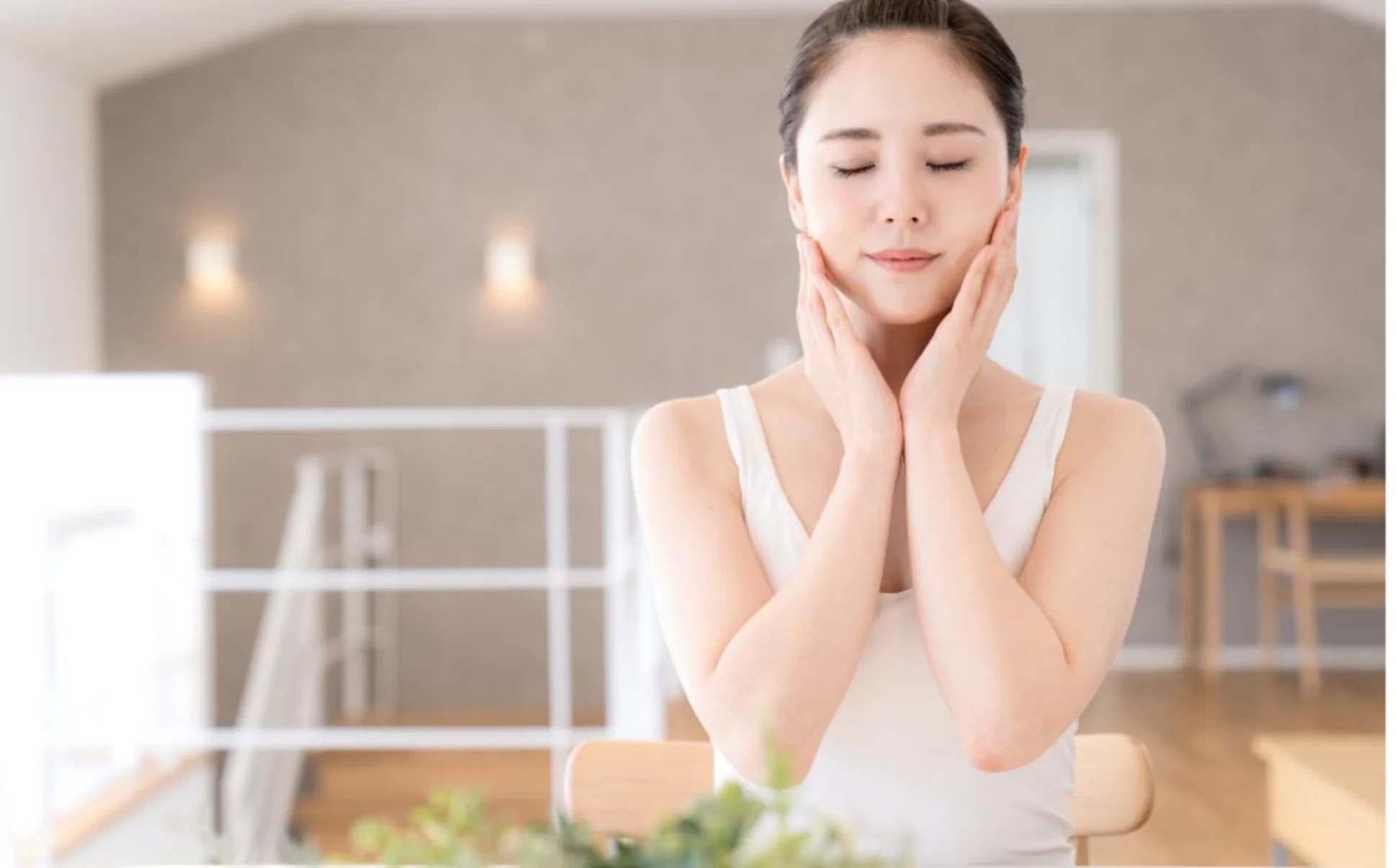 身穿白色背心的女子閉著眼睛,在一個安靜、燈光柔和的房間裡,用雙手輕輕地摸著自己的臉,暗示著放鬆與平靜。