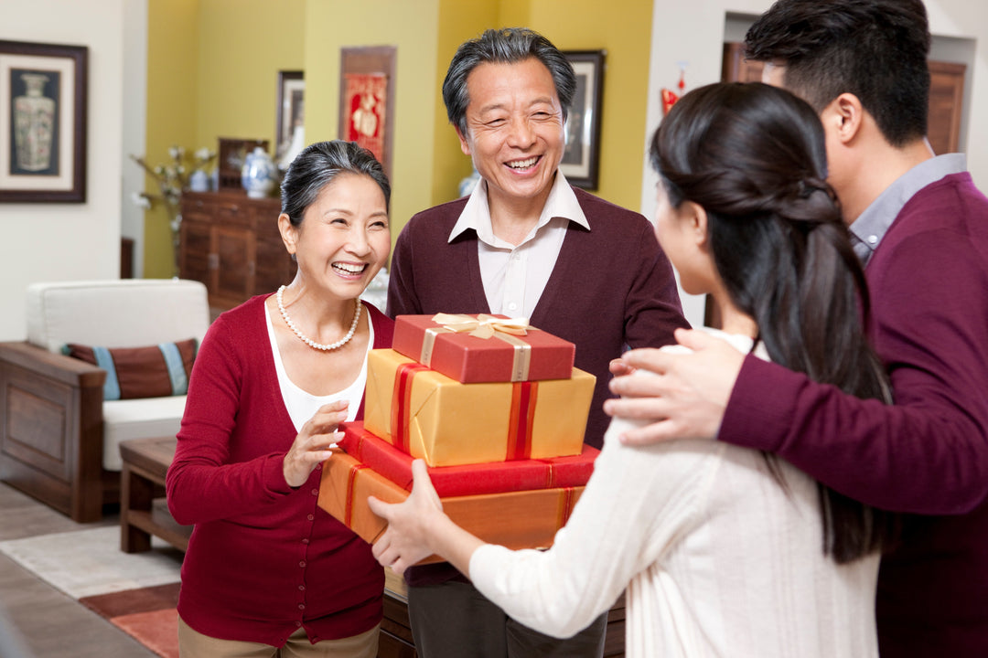 chinese young adult woman with husband providing gift for her chinese mother in law in living room