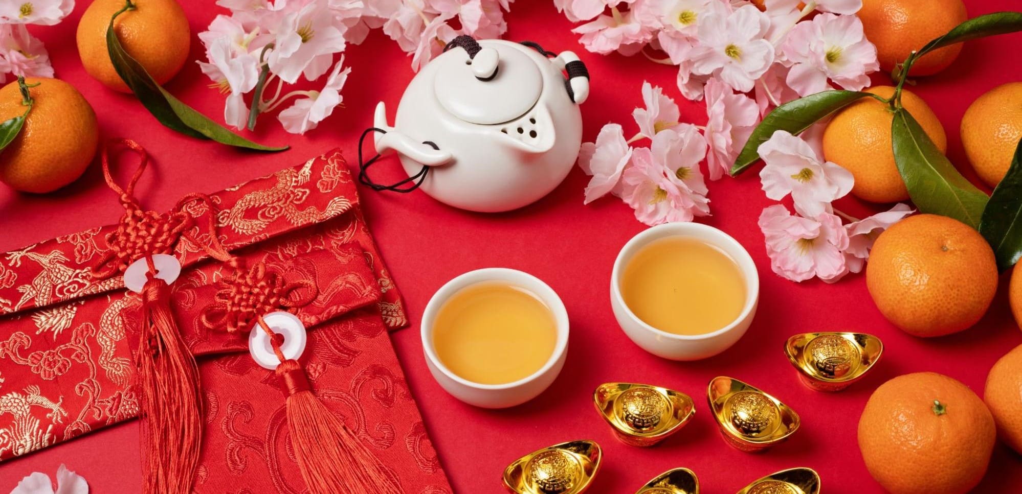 红底白色茶壶、茶杯、橘子、金锭、红包和粉色花朵的喜庆布置。